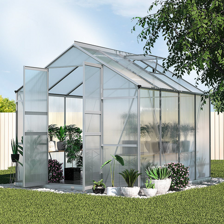 "Elegant polycarbonate greenhouse in a lush garden setting, featuring wide-open doors and abundant plants thriving inside."