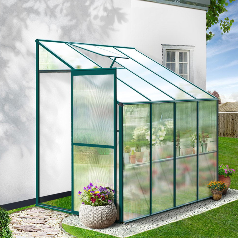 A compact greenhouse attached to the side of a house, surrounded by a well-maintained garden, providing an ideal space for plants.