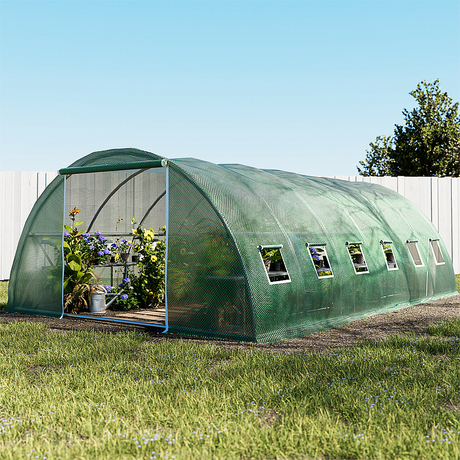 Large walk-in greenhouse tunnel with green mesh cover, containing blooming flowers and plants inside