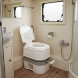 the portable toilet placed in a real-world setting, likely inside an RV, caravan, or small boat bathroom. It is situated on a wood-effect floor near a small sink and window.