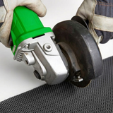 A worker in protective gloves uses a green angle grinder to cut through a sheet of black metal bushfire-rated mesh.
