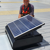 Worker standing beside a newly installed solar roof ventilator on a large rooftop.
