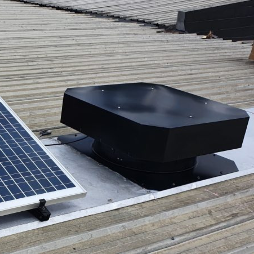 Black solar roof ventilator mounted on a metal roof beside a large solar panel.