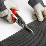 Gloved hands use red-handled tin snips to manually cut through the durable black metal mesh screen for a custom fit.
