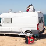 Red generator powering a caravan parked on a sandy site.