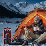 Person sitting by an orange tent in a snowy mountain landscape with a portable stove and coffee mug.